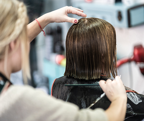 Stylist cutting client’s hair with scissors in front of salon mirror